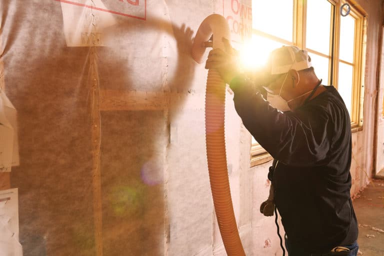 A installation technician blows loose fill insulation into the empty spaces of a wall during a new construction project