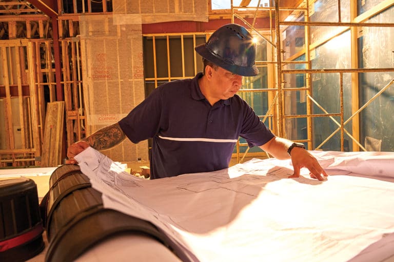 A foreman wearing a hard hat looks at plans for a new construction project