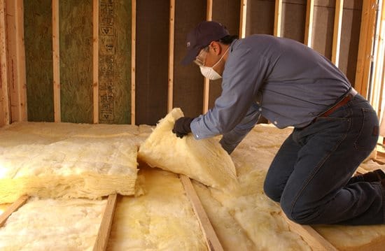 insulation installer placing fiberglass batt insulation in attic