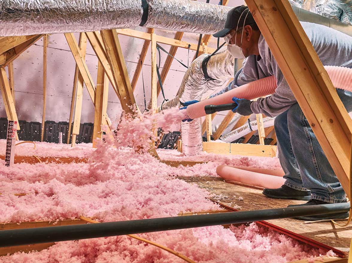 An insulation technician blows loose fill insulation into an attic