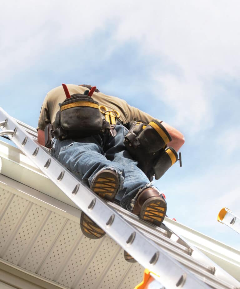 A worker standing on a ladder repairing a gutter system