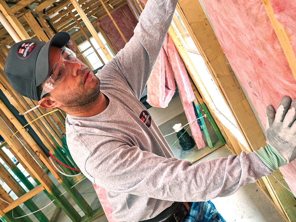 An insulation installer places fiberglass insulation in between wall supports