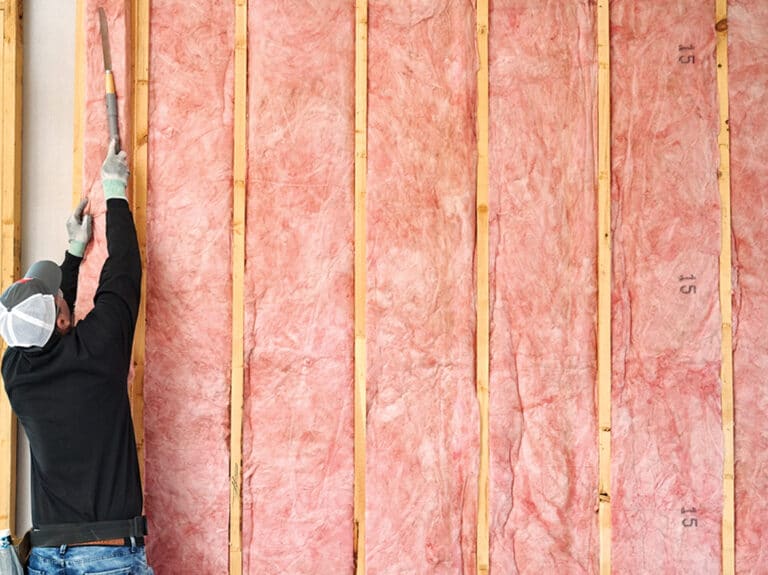 An insulation installer finishes placing fiberglass insulation in between wall supports