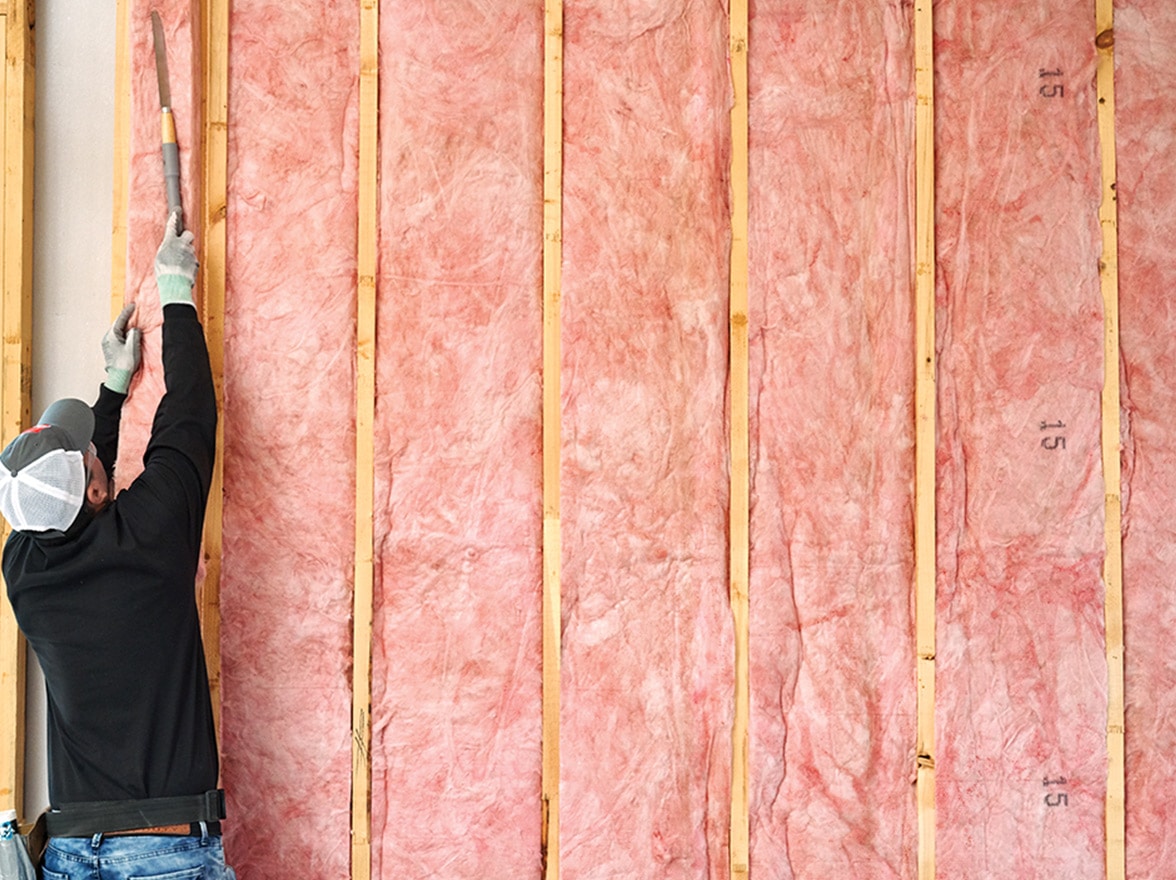 An installation technician filling an open wall with fiberglass batts