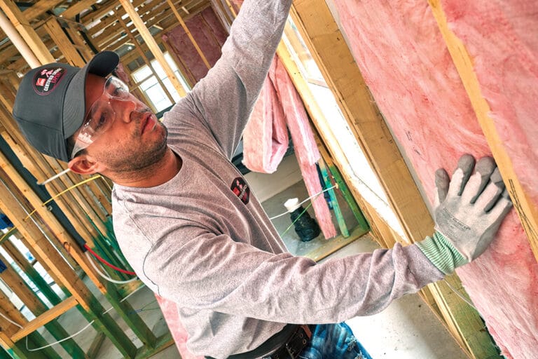 A worker installs batt insulation in a new construction project