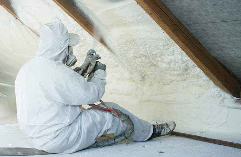 A technician using spray insulation to line the primary spaces of an attic